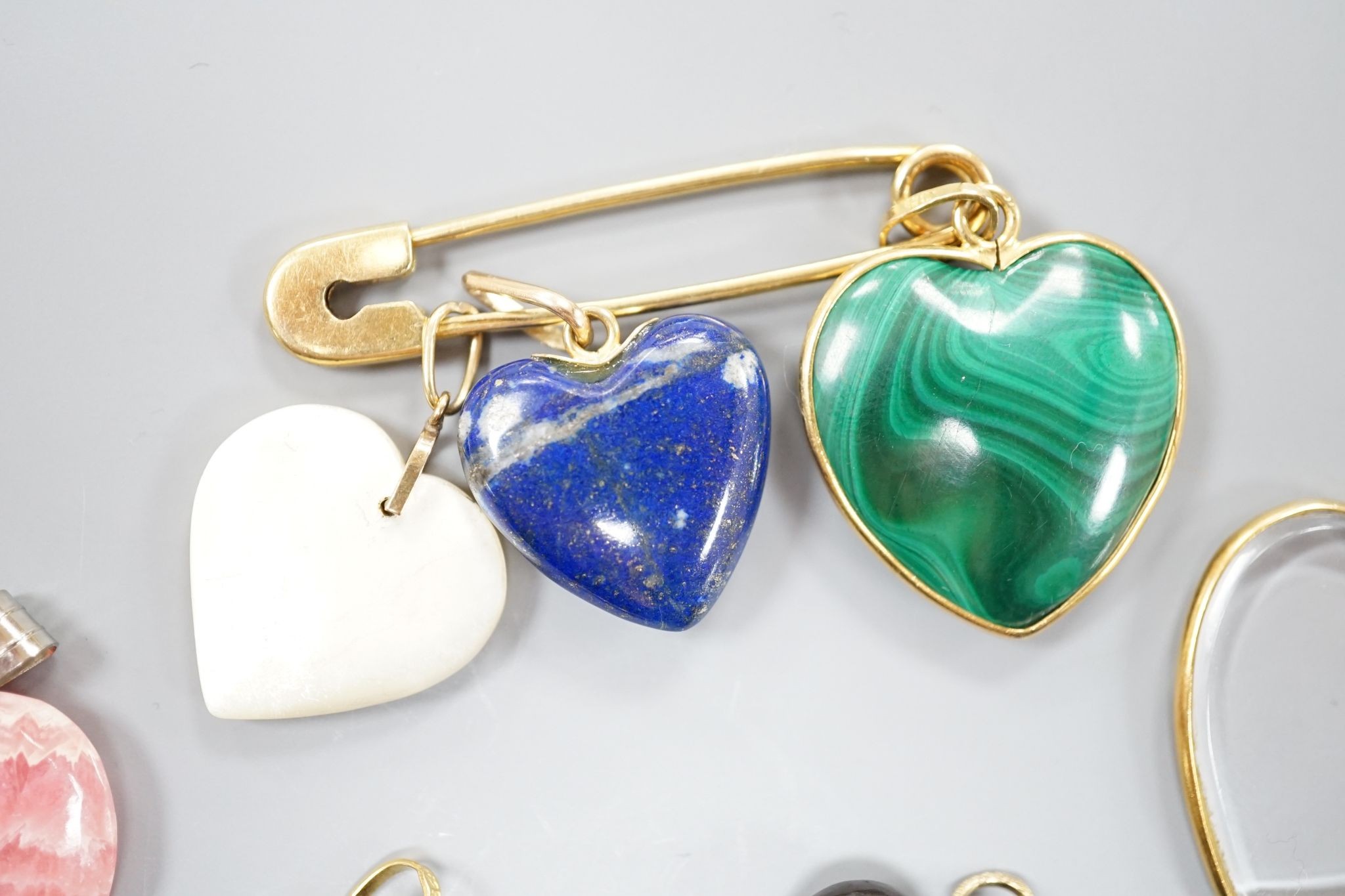 An 18ct safety pin, 47mm, hung with seven assorted heart shaped hardstone pendants or charms, two with Italian 750 yellow metal mounts.